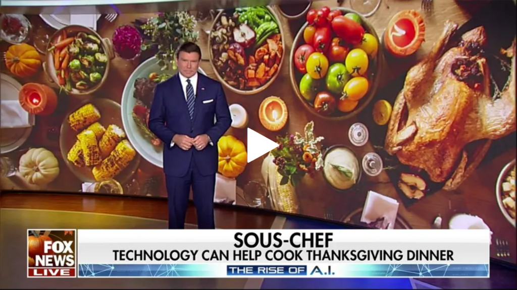 Scott Baier in a suit in a video frame in front of a screen with a background depicting a Thanksgiving meal